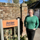 Lisa stands next to a brick wall with an orange sign which says Amber Farm Place in navy text. 