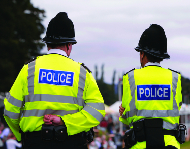 Two police officers pictured with their backs to the camera. They are wearing high vis jackets with "POLICE" written across their backs.